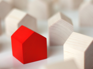 Photo of a red wooden house among other wooden houses (Adobe Stock photo).