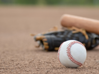 Photo shows a baseball, bat and glove on a baseball field (stock photo).